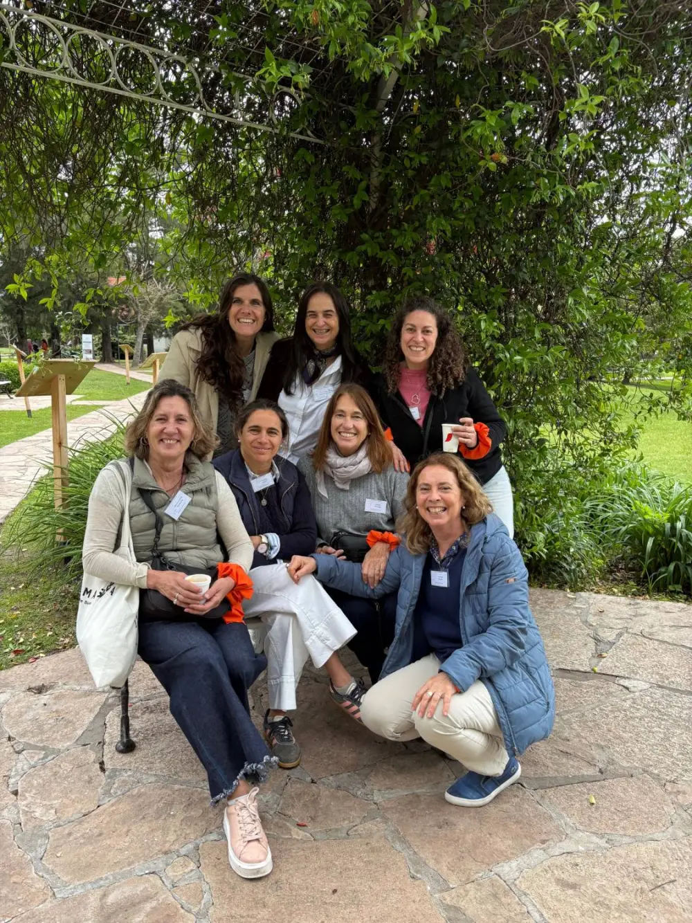 Siete mujeres del Grupo de Madres de Melipal, sonrientes, en un jardín bajo una pérgola con enredadera